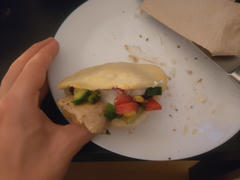 Eine aufgeschnittene und gefüllte Arepa auf einem Teller, meine Hand hält sie hoch.