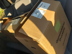 A view of the back seat of a car loaded with the large cardboard boxes. The boxes are labeled, and sunlight streams in through the windows.