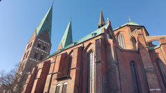 Aufnahme der Marienkirche aus der Froschperspektive: eine gotische Kirche aus rotem Backstein mit hohen grünen Kupfertürmen und Bogenfenstern vor einem strahlend blauen Himmel.