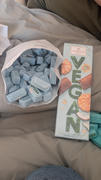 Eine Tüte mit einzeln verpacktem blauem Niederegger-Marzipan ist auf ein beiges Sofa neben einer Schachtel mit der Aufschrift „Niederegger Lübeck“ – vegane Kokos-Makronen-Schokolade – verschüttet.