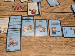 A collection of cards laid out on a wooden table from Star Munchkin. The cards feature colorful, cartoon-style illustrations, some with text describing game abilities or bonuses. Playing tokens and a die are also visible on the table.
