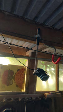 In einem kleinen Schuppen befindet sich eine Kamera aus einer Plastikschale um einen Raspberry Pi, an der die Pi-Kamera festgeklebt ist. Sie ist am Ende eines Selfie-Sticks befestigt, der an einem Holzbalken angebracht ist.